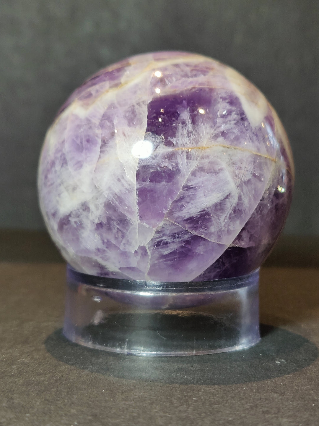 Polished amethyst sphere sculpture close-up on clear acrylic base, deep purple core