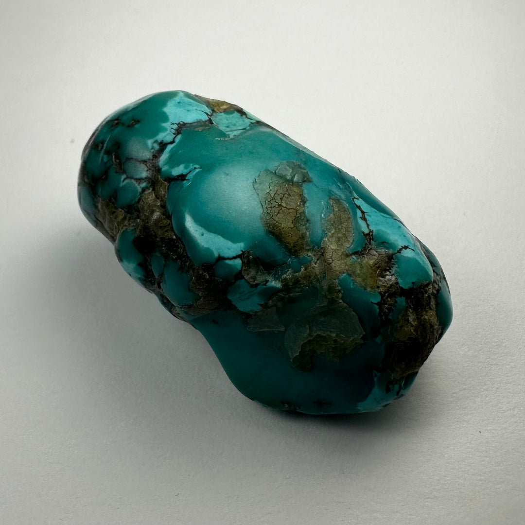 Turquoise nugget with teal surface and dark mineral patches, rounded elongated shape.