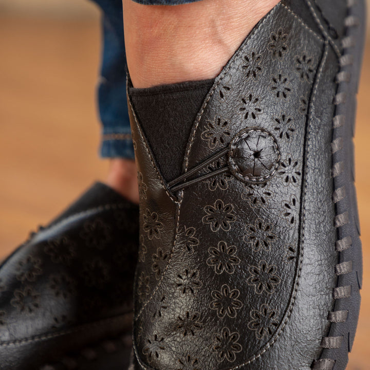 Close-up of dark slip-on loafer with embossed floral perforations and stitched side panel