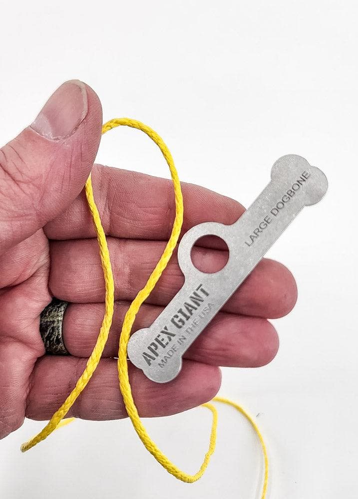 Metal large dogbone bag toggle with yellow cord loop, held in hand