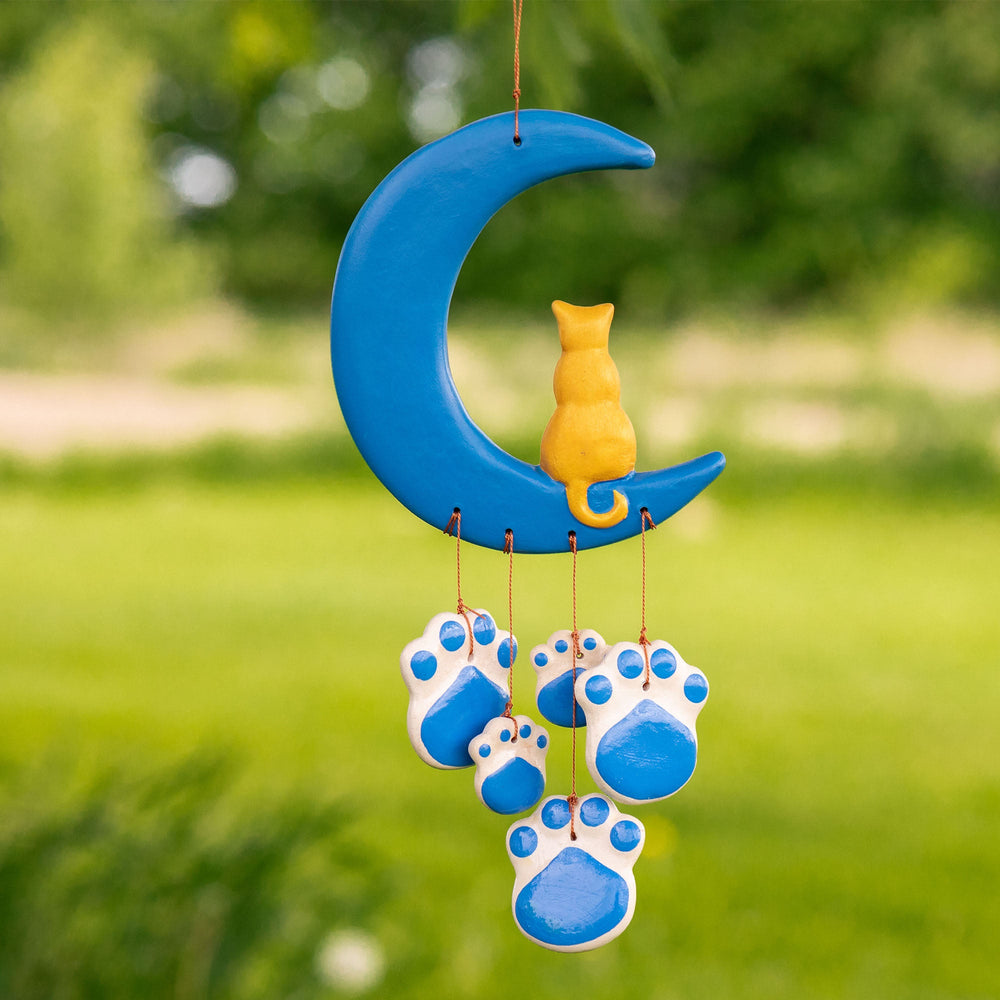 Blue ceramic cat paw moon wind chime hanging outdoors with three paw discs and center cat