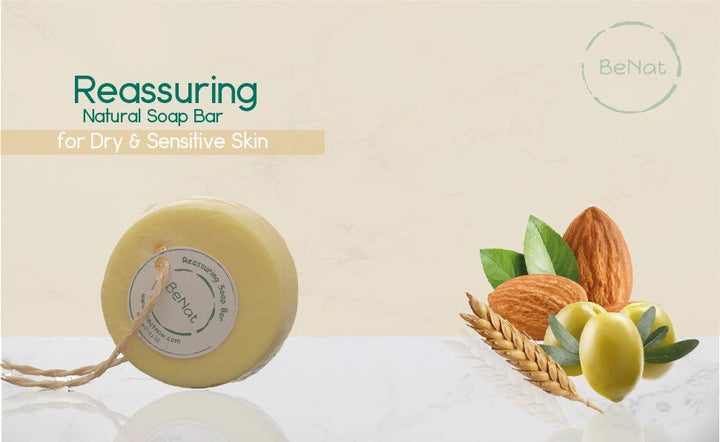 Round pale yellow soap bar with hanging tag, alongside illustrated wheat and olive oil items.