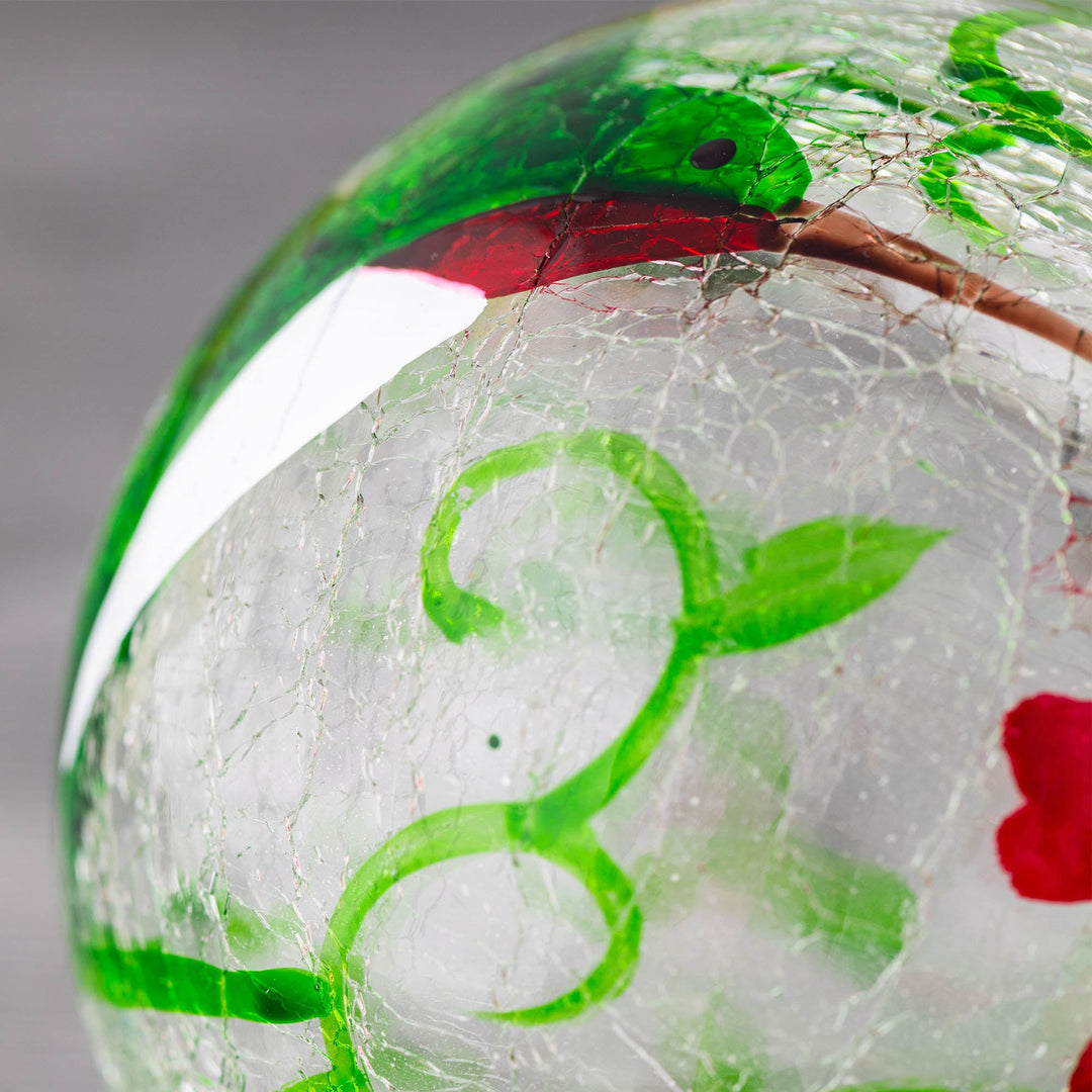 Hand-painted glass feeder close-up with green vine, red details, and cracked glass