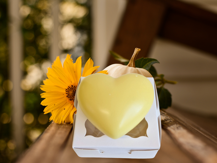 Yellow heart-shaped wax sachet in a white box beside a sunflower and greenery