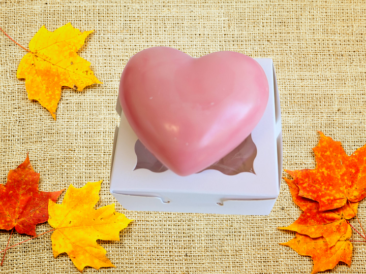 Pink heart-shaped wax sachet in a white box on a burlap-like fabric with leaves