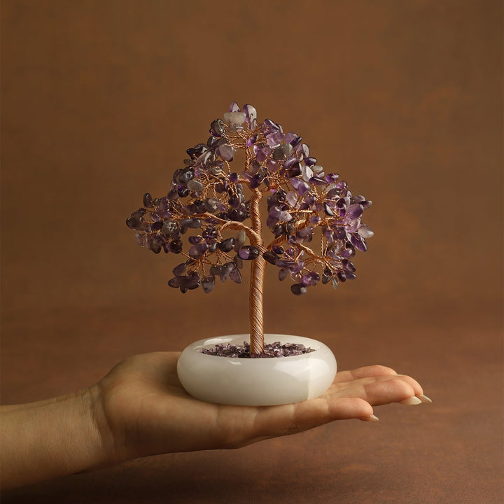 Amethyst crystal tree with gold-toned wire trunk and round white base held in hand