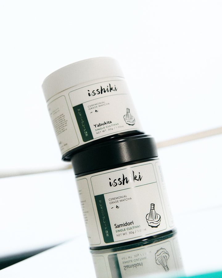 Stacked ceremonial matcha powder jars with black lids on a light surface.