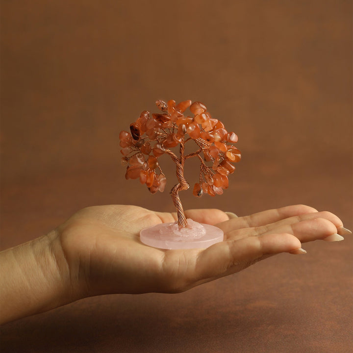 Orange crystal tree ornament held in a hand on a small pink round base