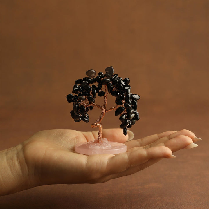 Black gemstone mini crystal tree on pink stone base, held in open palm