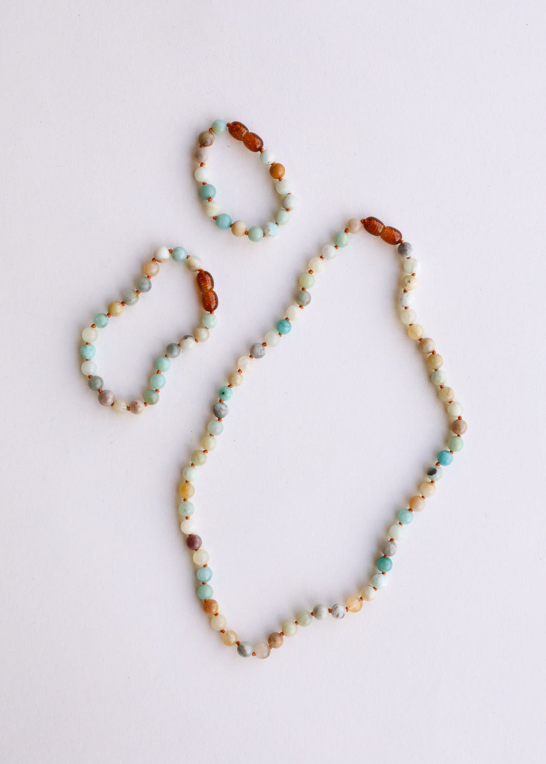 Set of beaded necklaces laid on flat surface, showing white and aqua round beads with brown spacers.