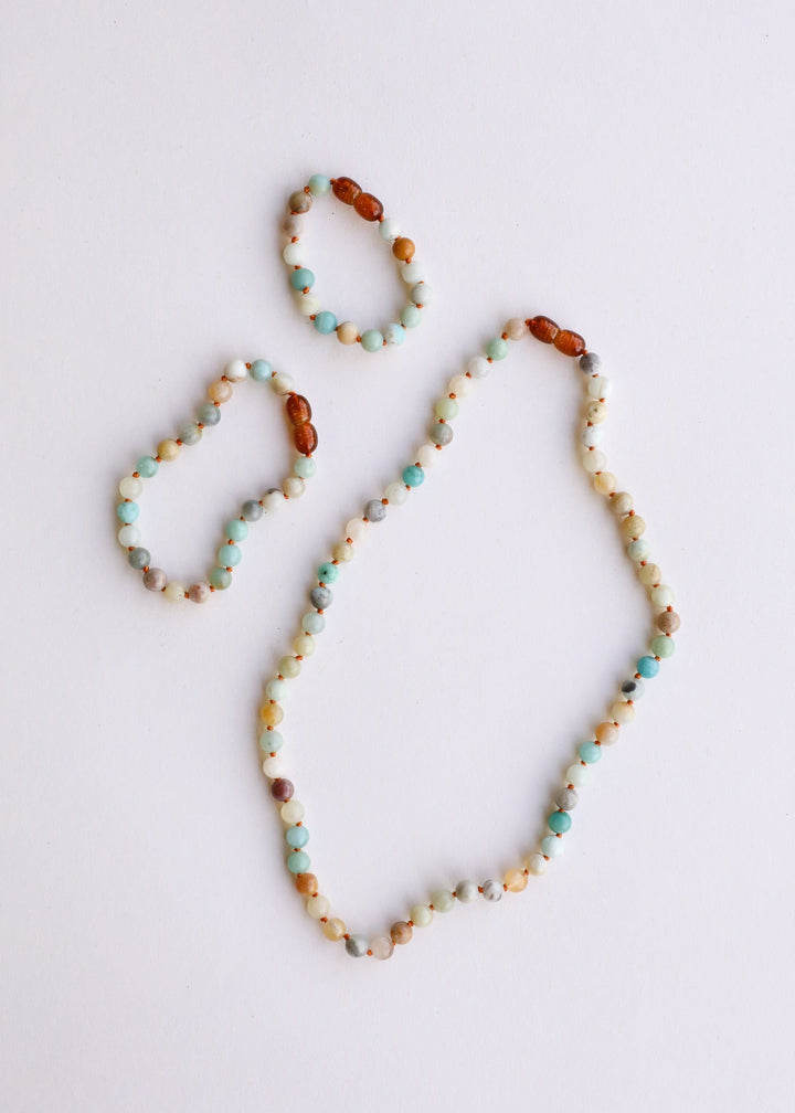 Set of beaded necklaces laid on flat surface, showing white and aqua round beads with brown spacers.