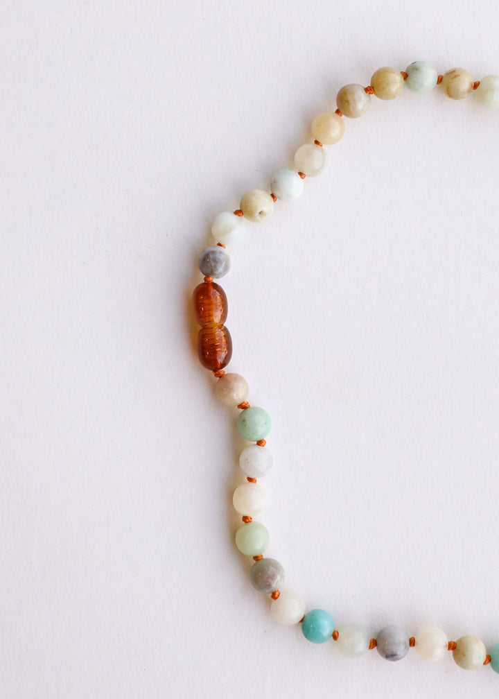 Partial view of beaded necklace with white, aqua, and peach beads and brown accent beads.