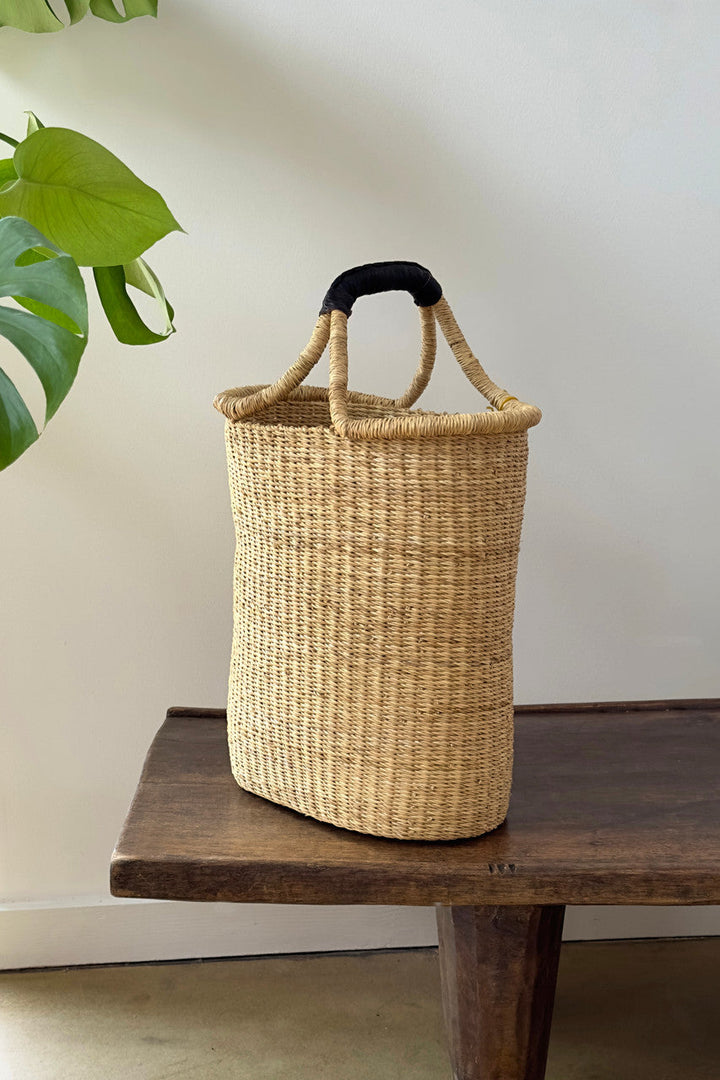 Woven pot basket with single arched handle, natural straw color and dark handle grips