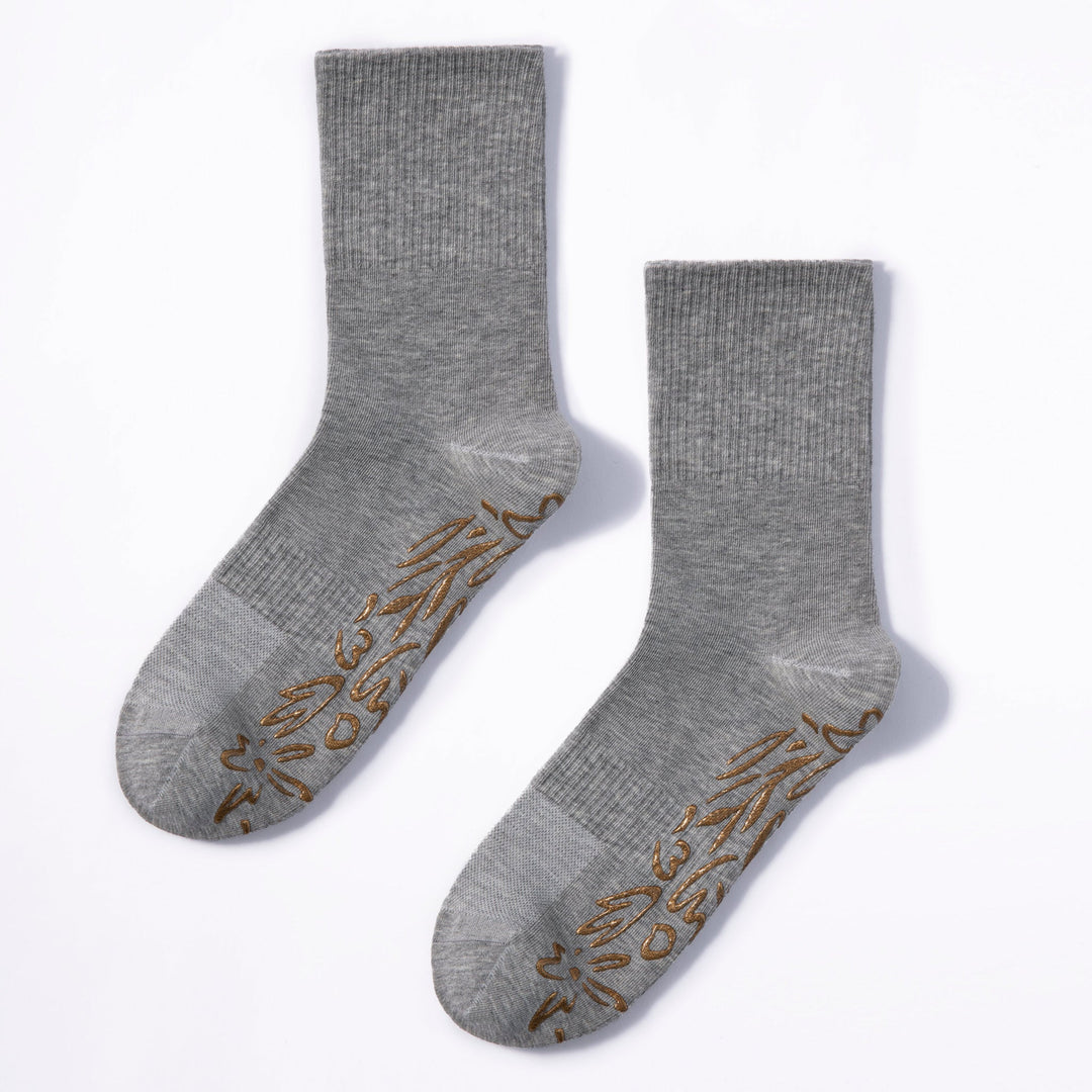 Pair of grey crew socks with gold floral non-slip grip on foot soles