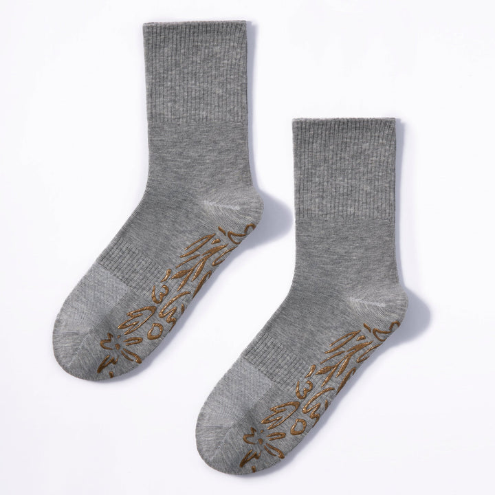 Pair of grey crew socks with gold floral non-slip grip on foot soles