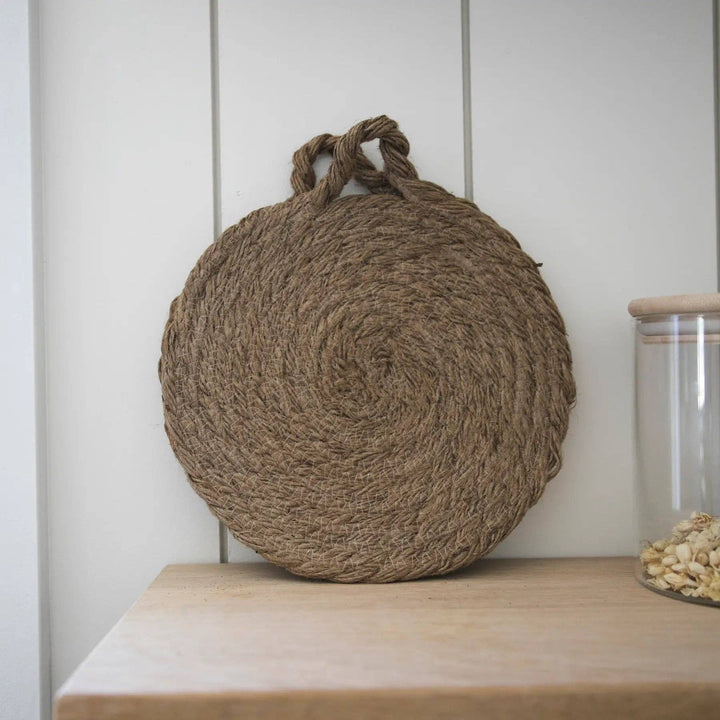 Round woven natural trivet with handle loop, displayed upright on shelf