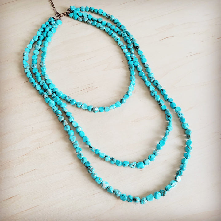 Turquoise triple-strand beaded necklace looped on display, brown chain ends