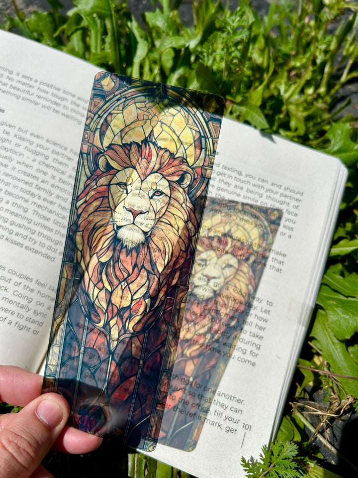 Lion face stained-glass style bookmark with blue border, held in hand over open book