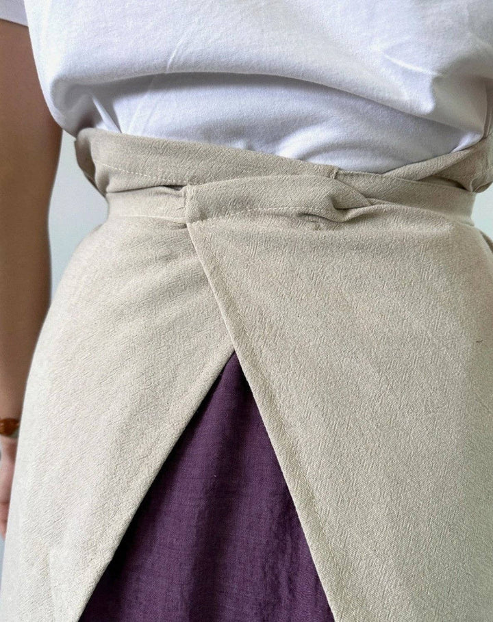 Light gray linen half apron close-up with gathered waist tie and diagonal front opening