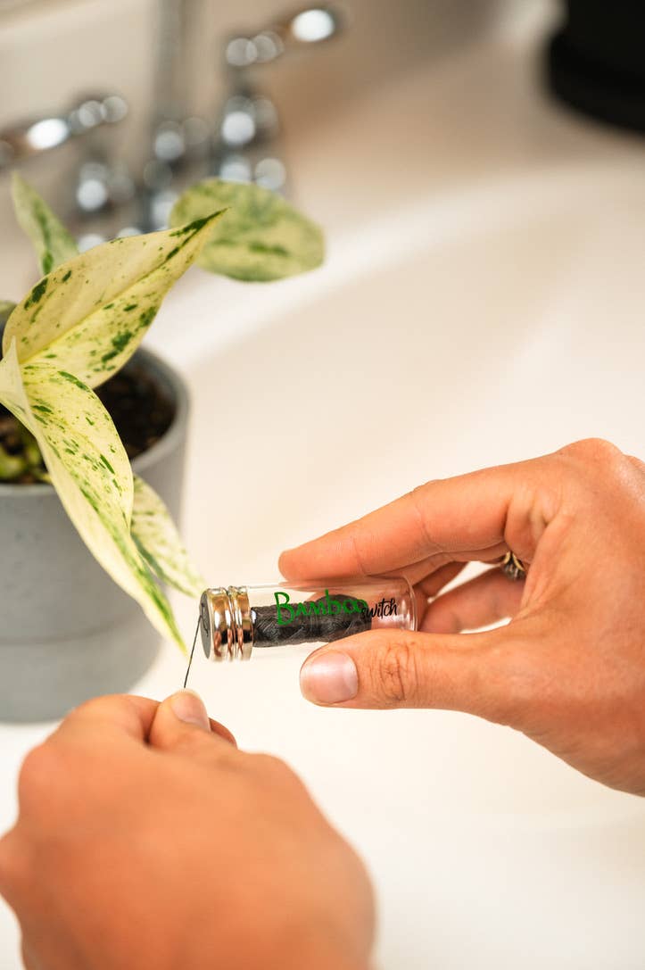 Bamboo floss in glass vial with hands preparing floss for use