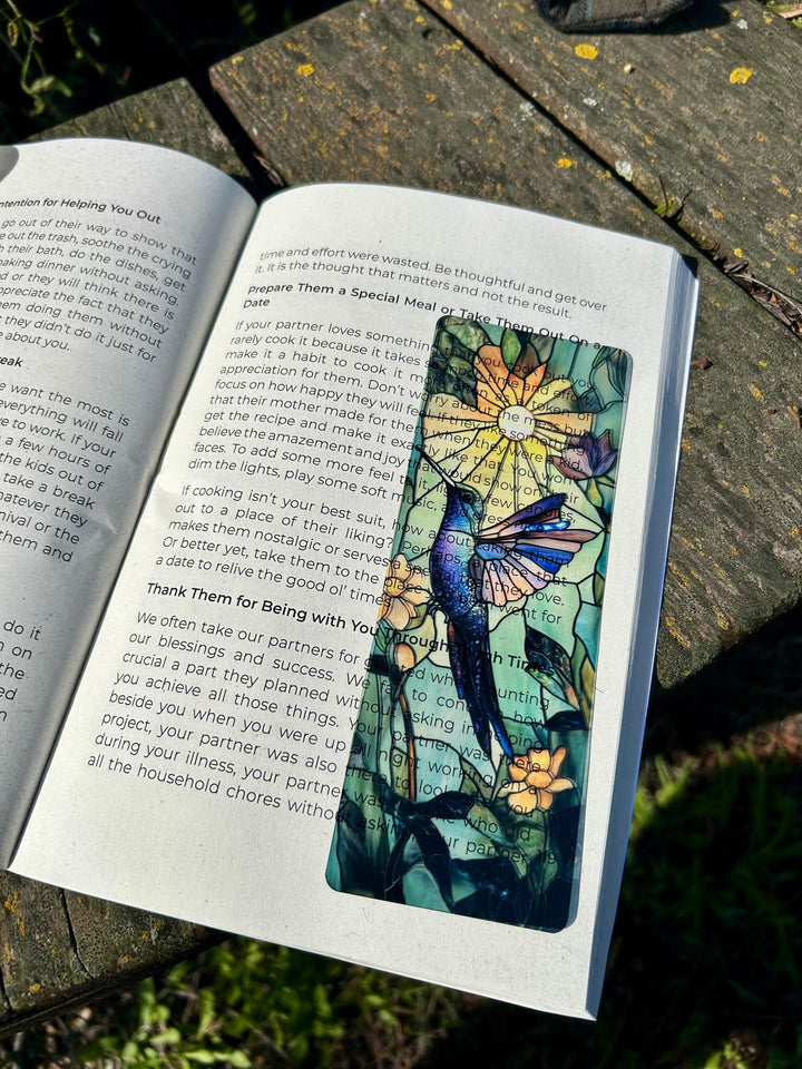 Hummingbird bookmark on open book page, colorful bird wings and flower motif