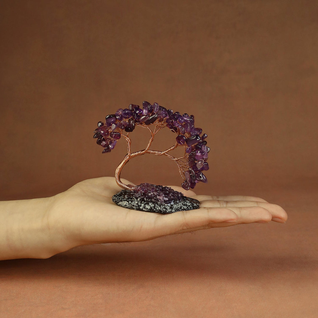 Purple gemstone crystal tree on a small stone base, held in a hand
