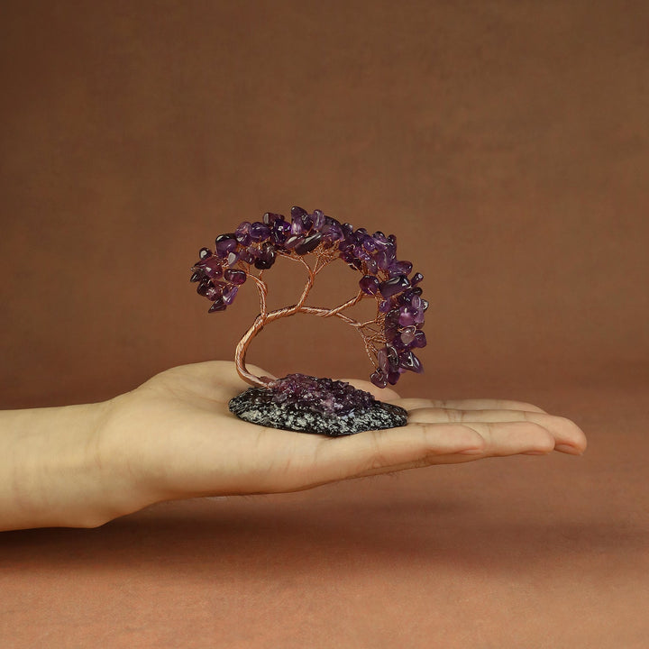 Purple gemstone crystal tree on a small stone base, held in a hand