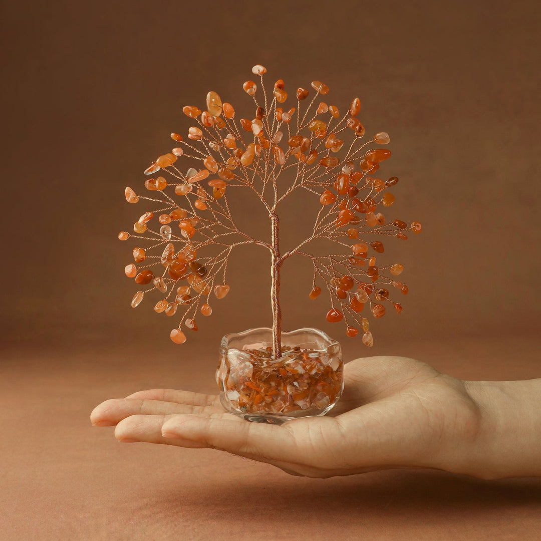 Orange crystal tree with wire branches on amber stone base, held in hand