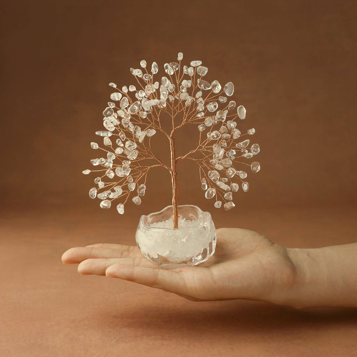 Clear quartz crystal tree with wire branches on white stone base, held in hand