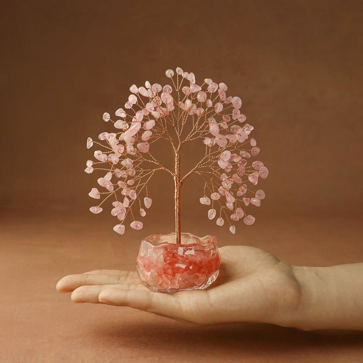 Pink crystal tree with wire trunk and gem leaves in red glass bowl, held in hand