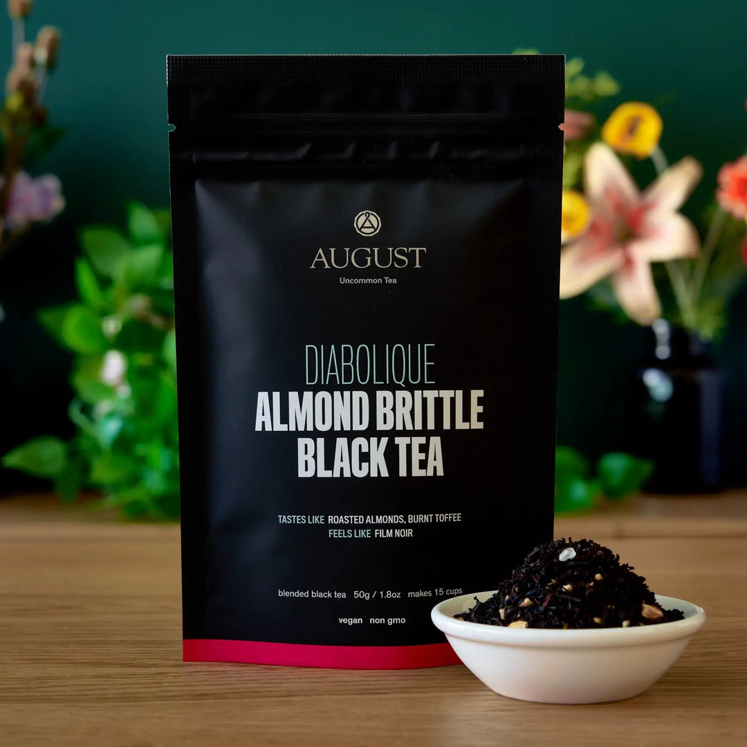 Black tea bag pouch with pink strip and bowl of dark loose tea leaves