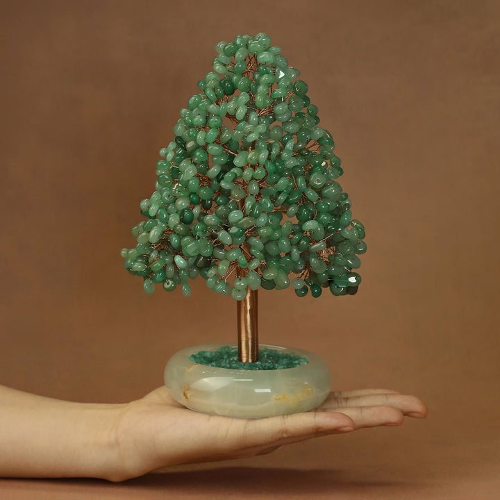 Green crystal tree ornament with gold-toned trunk on round white base, held in hand