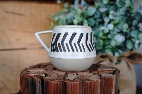 Two-toned geometric abstract ceramic mug, white with black arrow-like stripes, side view