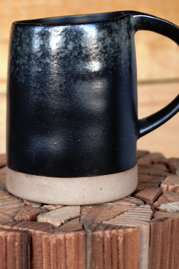 Black stoneware-style mug with tan base band and curved side handle