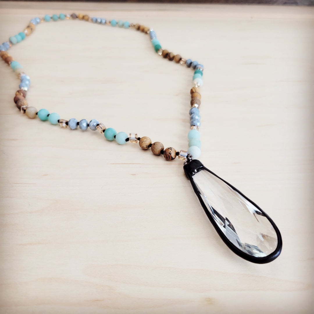 Long beaded necklace close-up: blue and tan beads with black-framed crystal drop