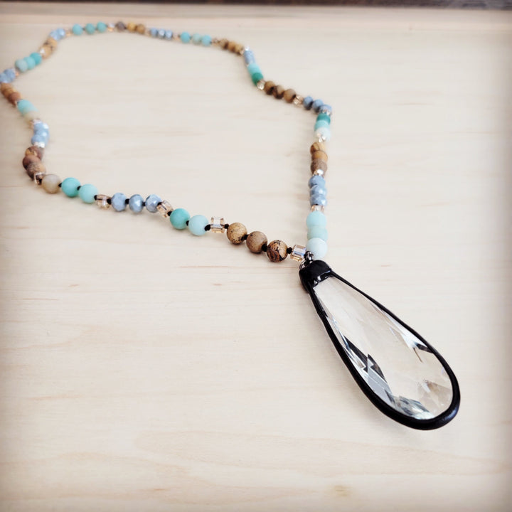 Long beaded necklace close-up: blue and tan beads with black-framed crystal drop