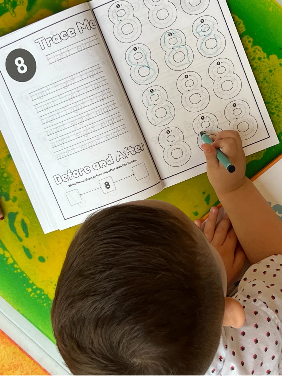 Open activity book page with large number 8 tracing lines and a child's hand