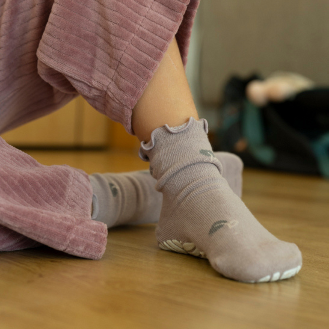 Toddler wearing gray non-slip socks with ruffled cuffs and small embroidered motifs