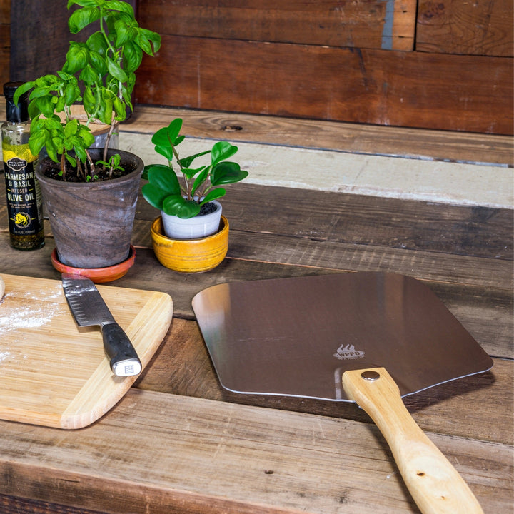Wood-handled pizza peel with dark metal board on wooden work surface