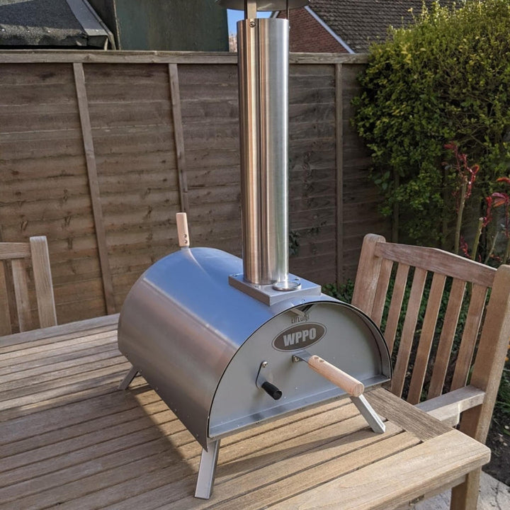 Stainless steel outdoor pizza oven on patio table, side view with control handle