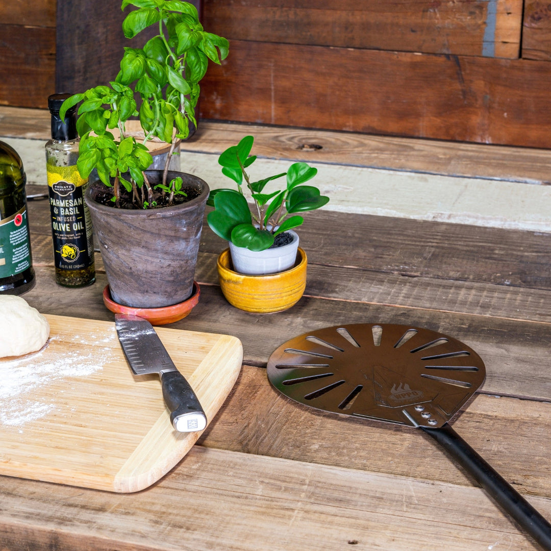 Round perforated aluminum turning peel with black handle on wooden board