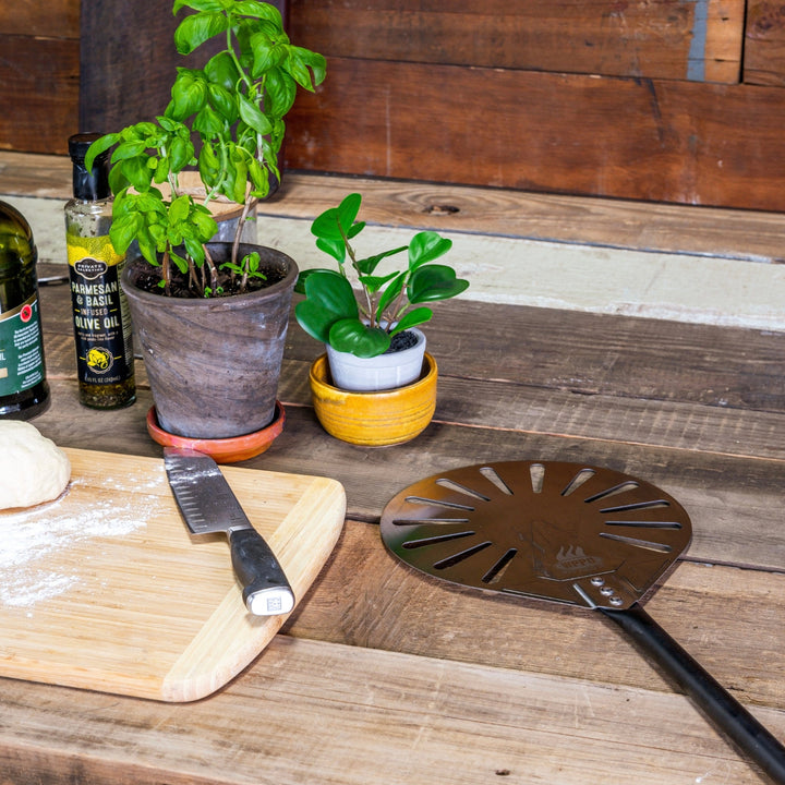 Round perforated aluminum turning peel with black handle on wooden board