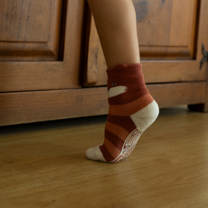 Rust-brown and striped non-slip crew socks with bear-face and swirl print, worn on feet