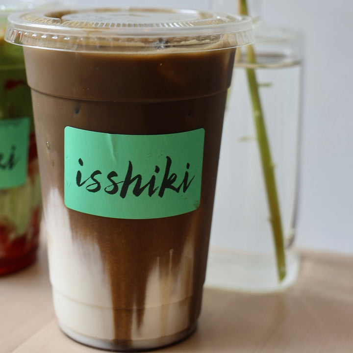 Iced hojicha drink in a clear cup with visible powder layers and paper seal