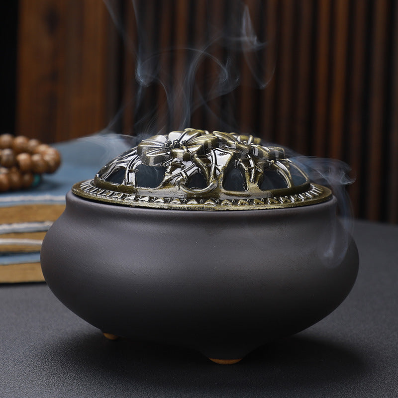 Ceramic incense burner with dark gray base and ornate gold-tone metal lid; smoke rising