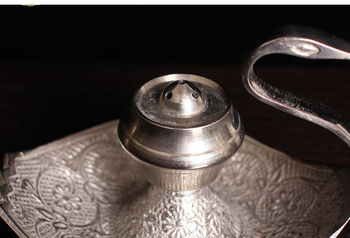 Close-up of silver-toned incense holder central cup and ornate engraved tray