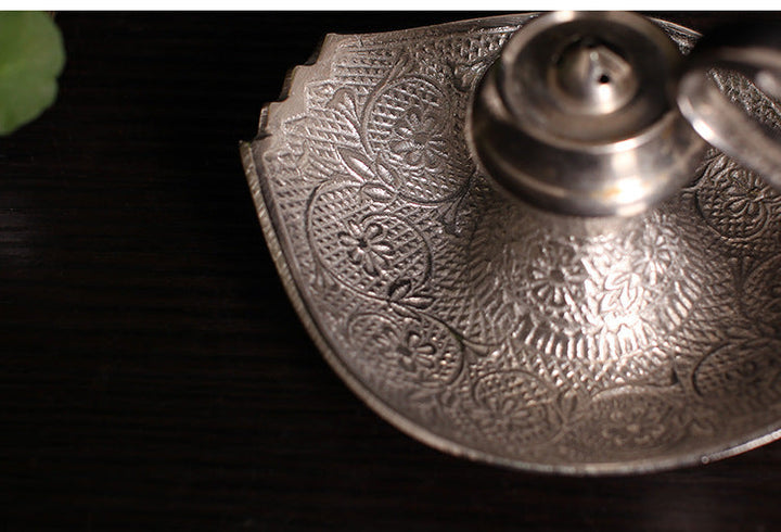 Close-up of silver-toned engraved tray and central incense cup on swan holder