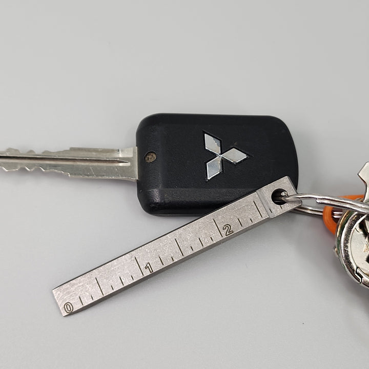 Keychain pry bar with black case, silver ruler markings, and orange lanyard loop