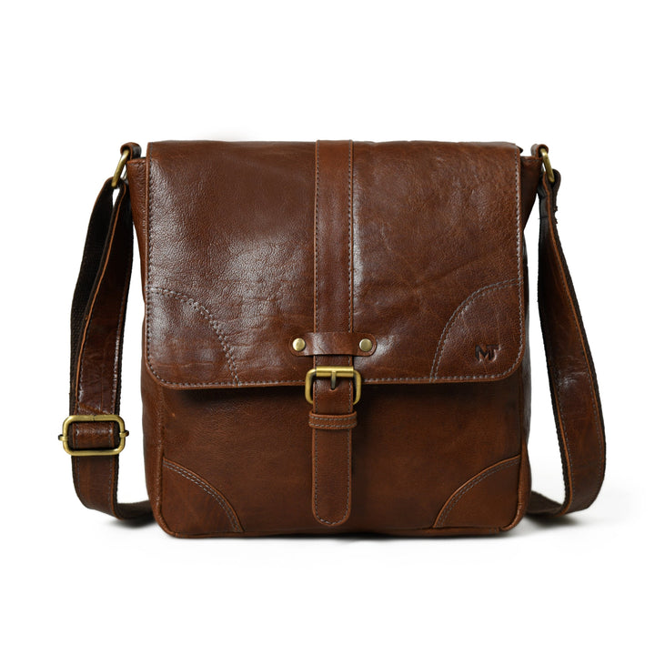 Brown leather unisex sling bag, front view with buckle strap and flap closure