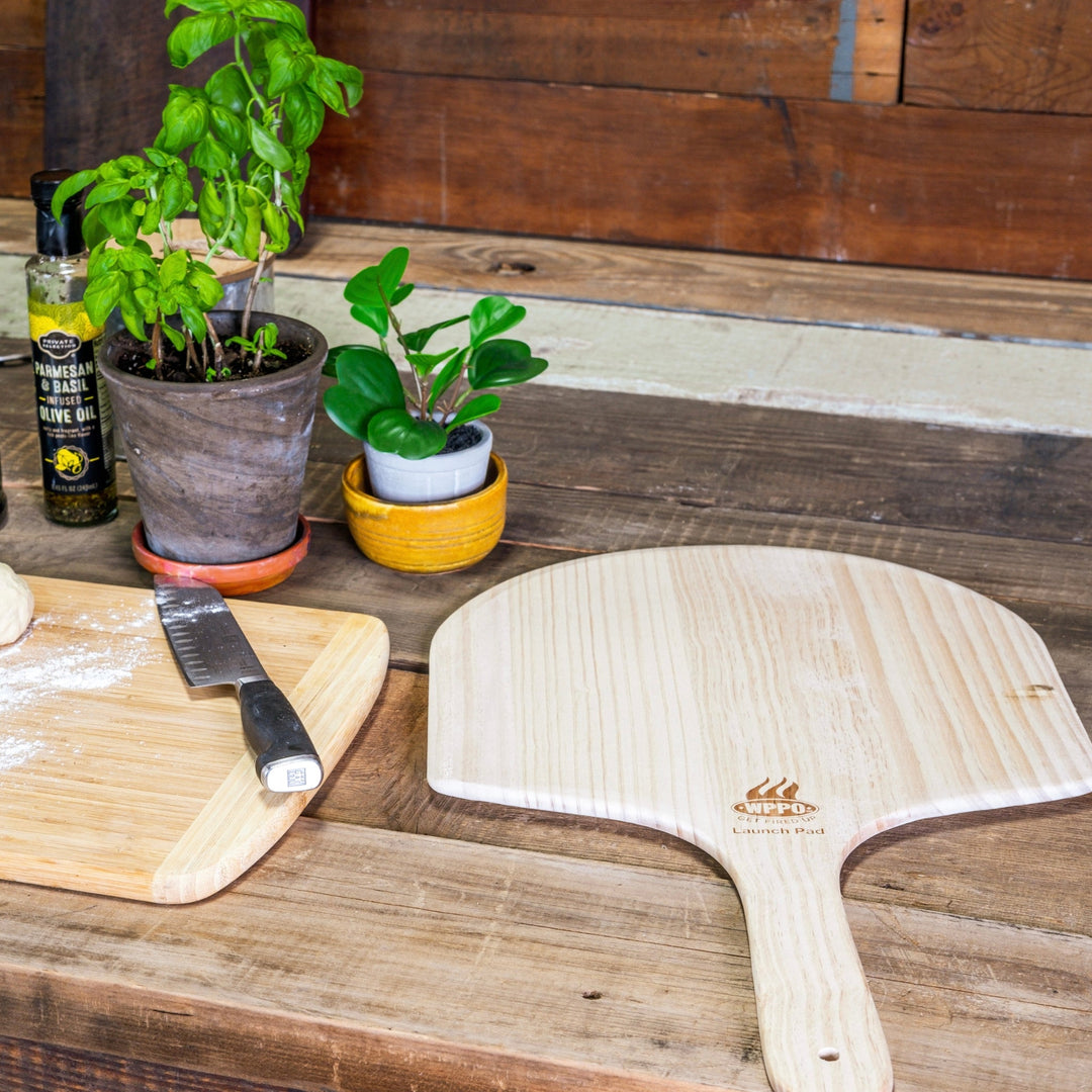 Two light wood pizza peels with rounded paddle and short handles on a tabletop.